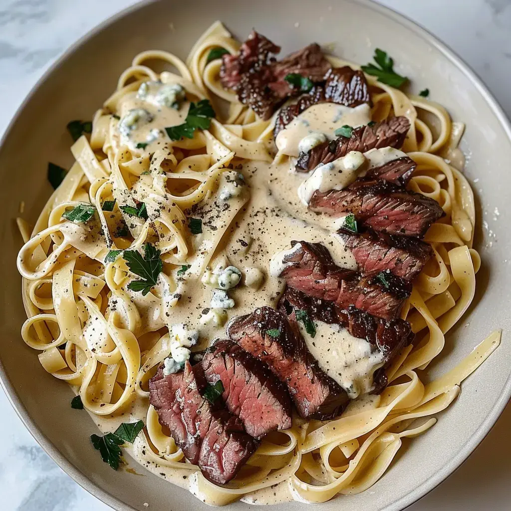 Ein Teller Fettuccine mit Steakstreifen und cremiger Sauce, garniert mit Petersilie und Blauschimmelkäse.