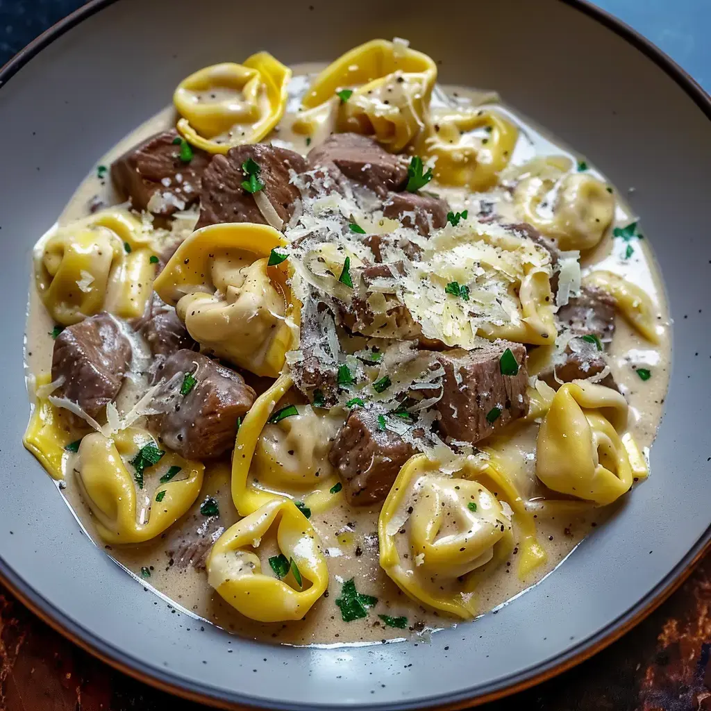 Ein Teller Tortellini mit Fleischstücken in cremiger Sauce, garniert mit geriebenem Käse und Petersilie.