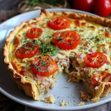 Herzhafter Kuchen mit frischen Tomaten, Kräutern und Fleischstücken, eine geschnittene Portion ist zu sehen.