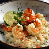 Ein Teller mit cremigem Garnelen-Risotto, garniert mit Limettenscheibe und Koriander.