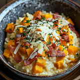 Eine Schüssel cremiges Risotto mit Stückchen Hokkaido, knusprigem Speck und geriebenem Käse.